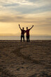 © J.Poquet - Two silhouettes of men on the beach. In a sunset with a calm sea.Friends holding each other by the back and raising an arm in joy.