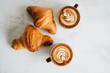 Two cups of coffee and croissant on white table
