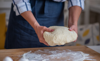 Cook hands kneading dough, piece of dough with white wheat flour. Low key shot, close up on hands, some ingredients around on table.