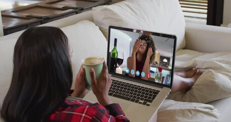 Sticker - Mixed race woman sitting on sofa using laptop making video call with female friend