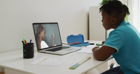 Canvas Print - African american boy doing homework while having a video call with female teacher on laptop at home