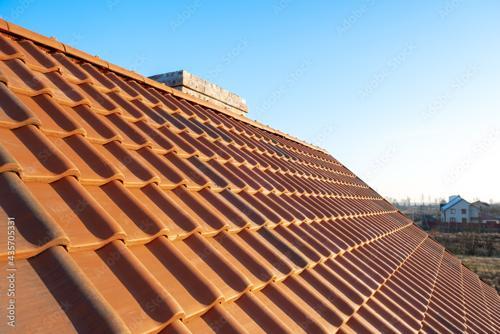 Overlapping rows of yellow ceramic roofing tiles mounted on wooden boards covering residential building roof under construction. - obrazy, fototapety, plakaty 