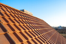 Overlapping Rows Of Yellow Ceramic Roofing Tiles Mounted On Wooden Boards Covering Residential Building Roof Under Construction.