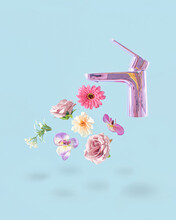 Creative Concept Of Pastel Purple Faucet From Which Fresh Pink Flowers Drip. Pastel Blue Background..