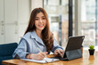 © amnaj - Asian Businesswoman beautiful long hair looking at the camera working using a tablet and documents at the office.