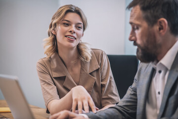 Cheerful young woman touching hand of serious male colleague