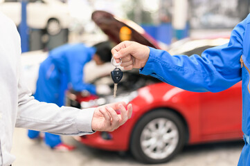 Car service, vehicle repair concept : Vehicle owner customer receiving car key from car service technician after sending his car for repairing or check at automobile service center.