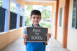 Smiling Young kid looking camera and showing by back to school sign board school at corridor - concept of school reopen and back to school.