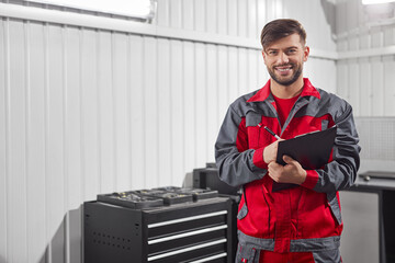 Smiling male mechanic taking notes on clipboard in workshop