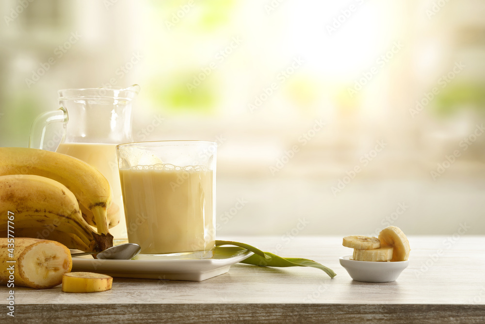 Milkshake with banana in glass cup on table kitchen background - obrazy, fototapety, plakaty 