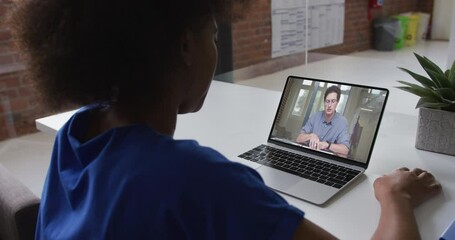 Poster - Back view of african american woman having a video call on laptop with male colleague at office