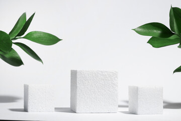 Wall Mural - white porous cube, square podium with leaves and shadows on a white gray background. conceptual scen