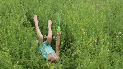 happy little girl lies in the grass, swinging her legs and blowing soap bubbles. outdoor recreation.