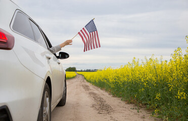 American flag in hand sticking out of the window of a white car. Independence Day of the United States of America. Pride, freedom, patriotism