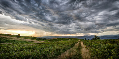 Dramatic storm scene with rain at the horizon and rural path going towards left.