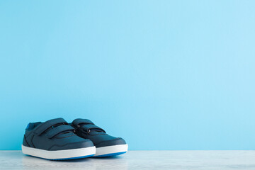 New dark sport shoes for little kid on wooden floor at light blue wall background. Pastel color. Baby footwear. Closeup. Front view. Empty place for text.