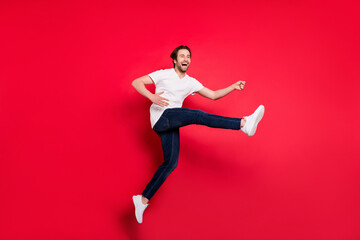 Full size profile side photo of young guy happy positive smile jump up play guitar artist isolated over red color background