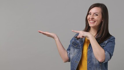 Wall Mural - Beautiful young promoter woman 20s years old in denim jacket yellow t-shirt pointing fingers hands aside on workspace copy space mockup promo commercial area isolated on grey color background studio