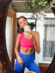 Pretty woman at home take photo selfie in mirror on mobile phone for stories and posts in social media, vertical frame, wearing sport wear, fit and slender, abs motivation