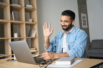 Wall Mural - Young happy indian arab eastern man talking on video conference call greeting waving hand using laptop at modern home office. Remote distant online communication technologies concept.