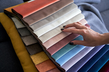 Wall Mural - Choosing upholstery fabric color and texture from various colorful samples in a store. Female customer hands touching textile.