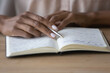 © fizkes - Close up young african american woman holding pen in hands, reading notes in copybook, repeating educational information preparing for exam. Focused mixed business lady managing assignments in planner