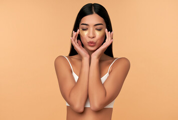 Wall Mural - Young Asian woman in white lingerie and clean radiant skin with moisturizing patches under the eyes on a beige background. Spa care, cosmetology.