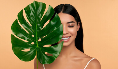 Young Asian woman in white lingerie and clean radiant skin with a green leaf on a beige background. Spa care, cosmetology. Natural cosmetics concept.