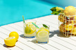 Homemade lemonade in glasses with lemon slice, basket of lemons, drinking straw,on white table,in the edge of the pool with turquoise blue water background,light and shadows, vocation 2021,summertime 