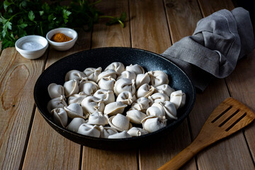 Wall Mural - A hearty lunch: frozen dumplings in a frying pan on a wooden table. Meat ravioli in a frying pan