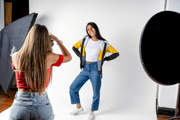 Photo session of a model and a woman photographer in a photography studio with flashes and a white background. Fashion concept.