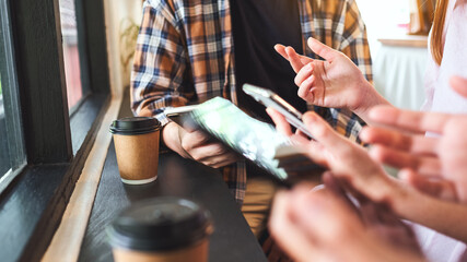 Wall Mural - Group of young people holding and using their mobile phones while sitting and talking together