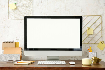 Modern computer and organizers on table near light wall