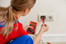 Young female electrician measuring voltage of socket at home