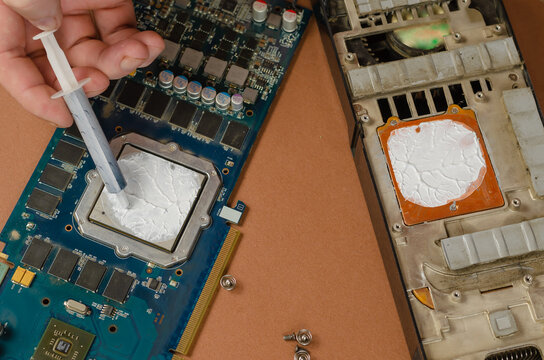 Computer graphics card on brown background. Man puts new thermal paste on the processor with a syringe.
