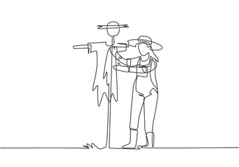 Poster - single continuous line drawing a young female farmer in a straw hat putting up scarecrow to keep out