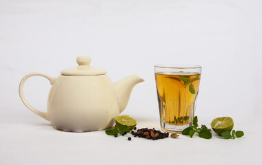 Poster - Closeup of a glass of herbal tea with lime and teapot on a white surface