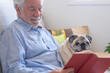 Portrait of clear purebred pug dog sitting with his senior owner on the sofa, relaxing  together at home