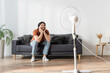 happy bearded man sitting on couch near blurred electric fan