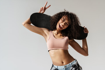 Young african woman snowing peace sign while posing with skateboard