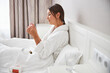© Viacheslav Yakobchuk - Charming Caucasian female with infrared thermometer and medicine pills in white modern bedroom