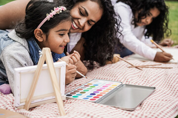Wall Mural - happy indian family having fun painting with children outdoor at city park - main focus on girl face