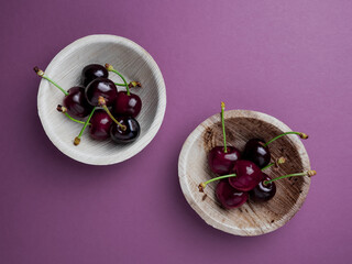 Wall Mural - ripe cherries on two bowls on pink background. top view. fresh red cherries with sprig and yellow flower. creative bright pink background. Food concept