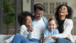 © fizkes - Overjoyed young multiracial family with two small daughters relax on sofa at home laughing joking. Happy multiethnic mom and dad rest together with small diverse children. Adoption concept.