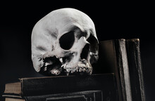 Photo Of Witchcraft Human Skull Laying On Old Books And Stacked Books On Black Background.