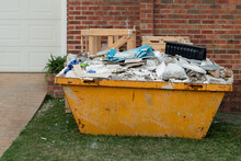 Skip Bin Full Of Household Waste Rubbish On The Front Yard. House Clean Up And Renovation Concept.