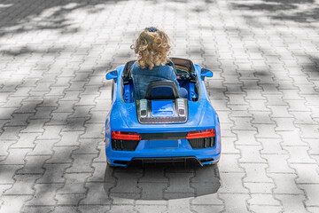 The child is driving a toy car in the park.