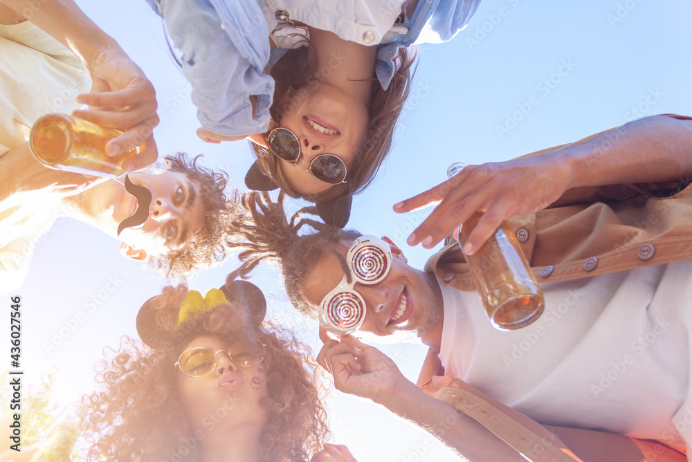 People stay in circle enjoying refreshing beverage. Young men and women drink beer on festival, birthday. Happy friends spending free time together in park sitting on grass, drinking beer and chatting - obrazy, fototapety, plakaty 