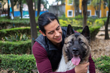 Young Hispanic Man Petting And Holding His American Akita Dog In The Park