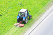 Tractor uses trailed lawn mower to mow grass on city lawns, aerial view.
